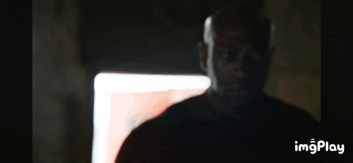 a man in a dark room with a red light behind him and the words imgplay on the bottom right