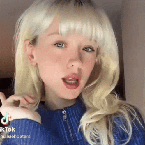a girl with blonde hair is wearing a blue sweater and a tiktok sticker