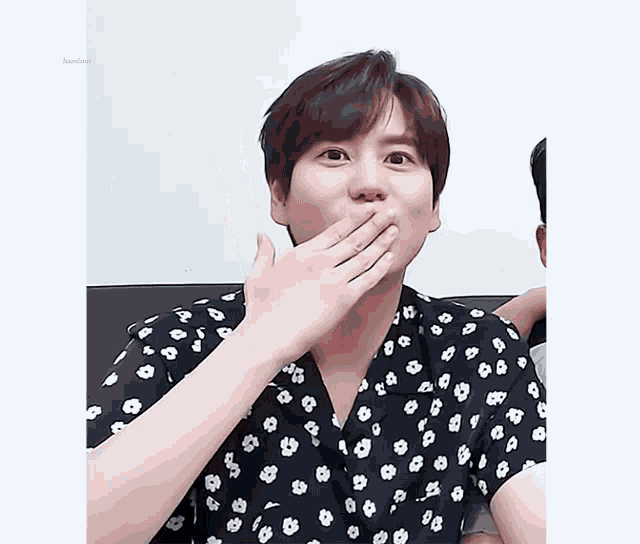 a man wearing a black shirt with white flowers covering his mouth with his hand