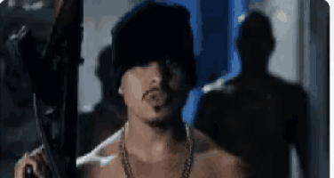 a man without a shirt is holding a gun and wearing a hat .