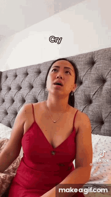 a woman in a red dress is sitting on a bed with her mouth open .