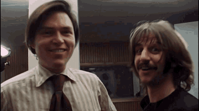two men standing next to each other smiling and looking at the camera
