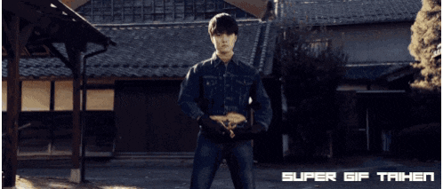 a man stands in front of a building with super gif taihen written on the bottom right