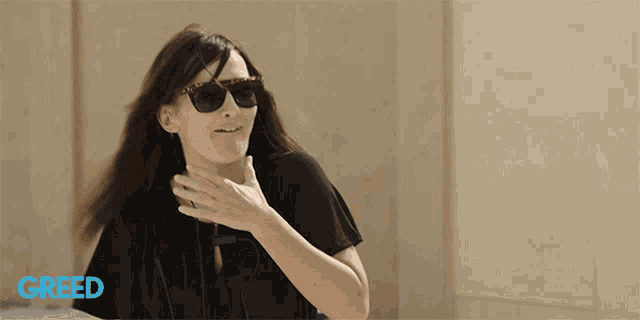 a woman wearing sunglasses and a black shirt with the word greed on the bottom