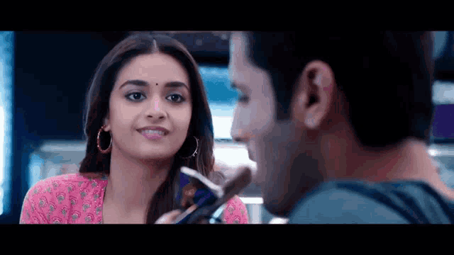 a man and a woman are looking at each other and smiling . the woman is wearing hoop earrings .