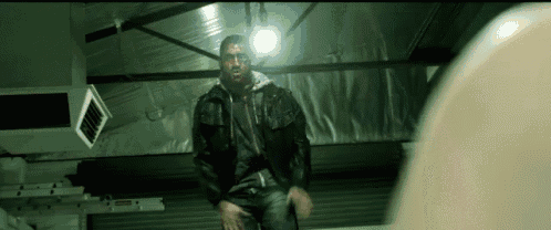 a man with blood on his face is standing in a dark room with a light on .