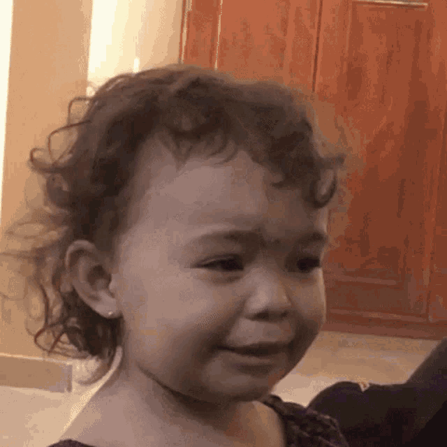 a little girl with curly hair is crying while sitting on the floor .