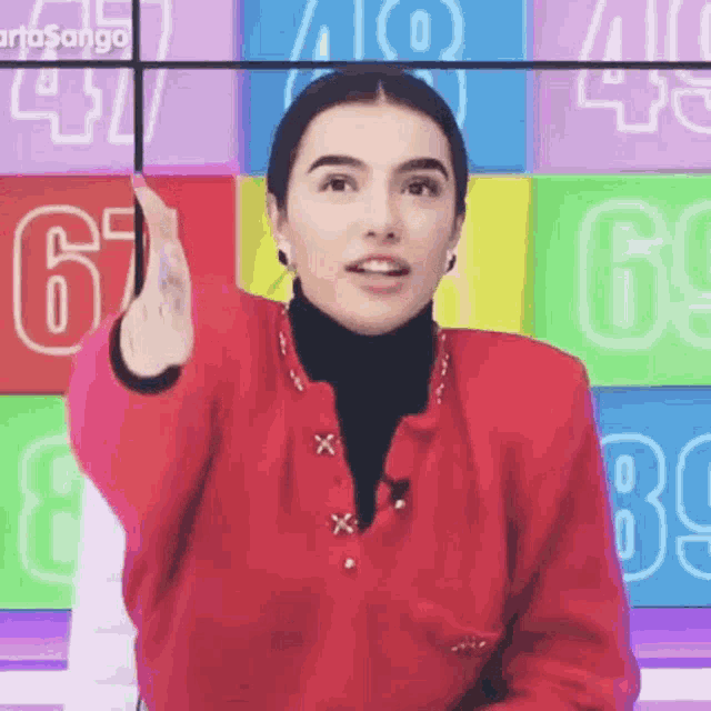 a woman in a red sweater and black turtleneck is pointing at something .