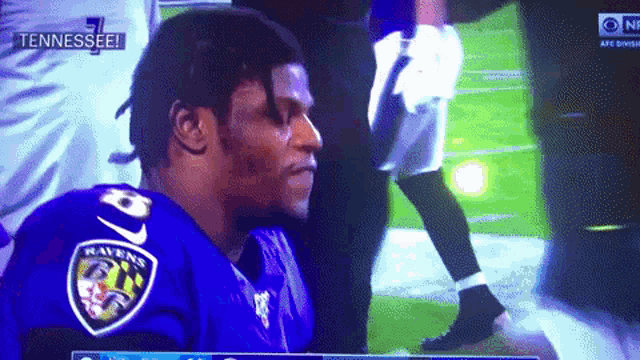 a man wearing a ravens jersey is sitting on the field