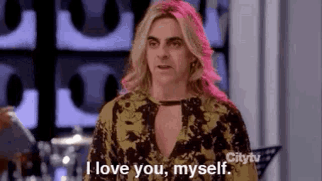 a woman with long blonde hair is standing in a room and saying `` i love you , myself . ''