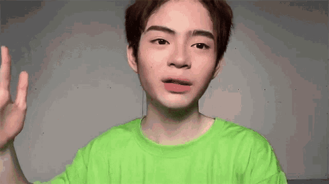 a young man wearing a green shirt is making a peace sign with his hand
