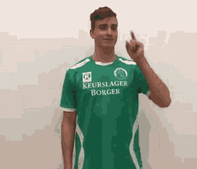 a young man is wearing a green shirt and giving the middle finger .
