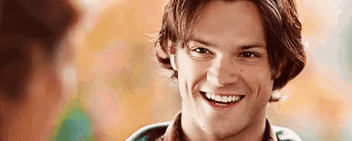a close up of a young man smiling with a blurred background