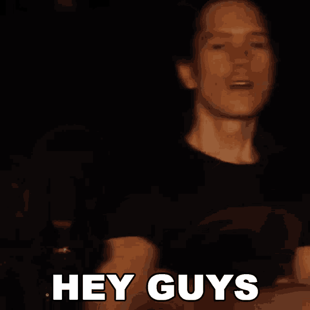 a man in a black shirt says hey guys in front of a microphone .