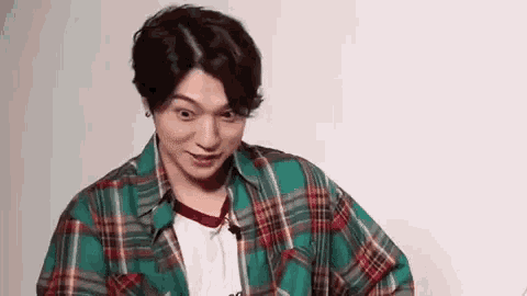 a young man wearing a green plaid shirt and a white shirt is making a funny face .