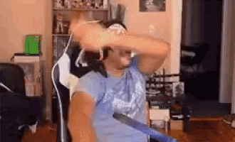 a man in a blue shirt is sitting in a chair in a living room holding a sword .