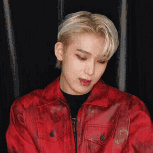 a young man with blonde hair is wearing a red jacket