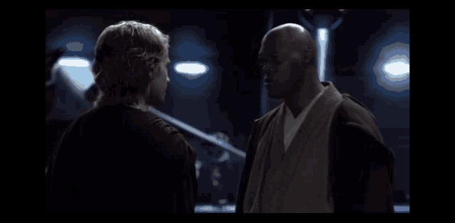 two men standing next to each other in a dark room looking at each other