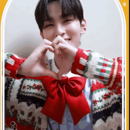 a man wearing a christmas sweater and a red bow making a heart shape with his hands
