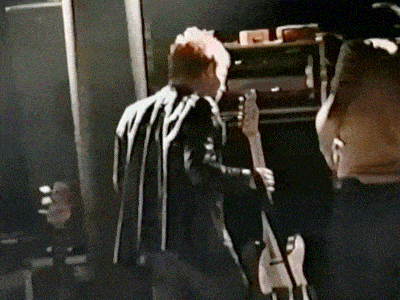 a man is playing a guitar in a dark room while another man watches .