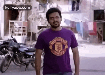 a man wearing a purple manchester united t-shirt is standing in front of a motorcycle .