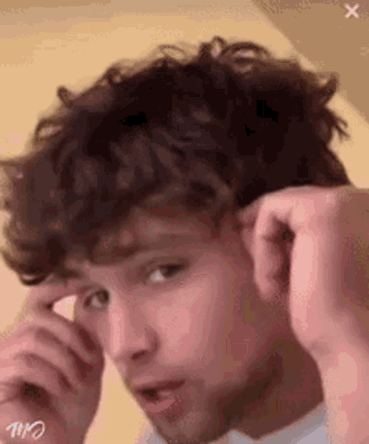 a young man with curly hair and a beard is adjusting his hair .