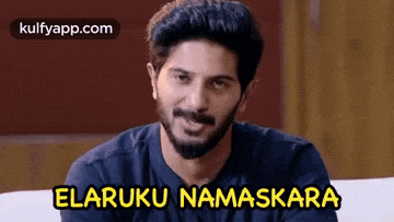 a man with a beard is sitting on a couch with the words elaruku namaskara written above him .