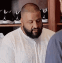 a man with a beard is wearing a white shirt and talking to another man in a room .