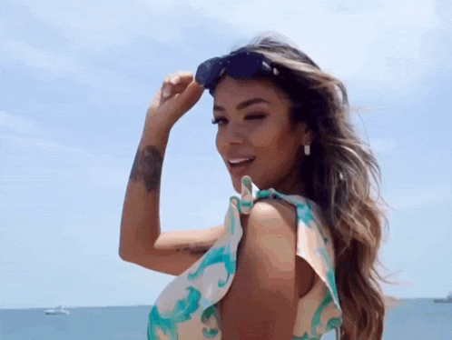 a woman wearing sunglasses is standing on a beach with the ocean in the background