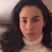 a woman with long dark hair wearing a white turtleneck sweater