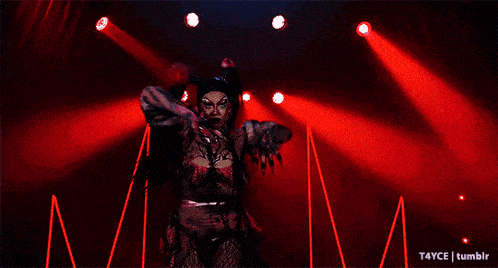 a drag queen is performing on a stage with red lights behind her ..