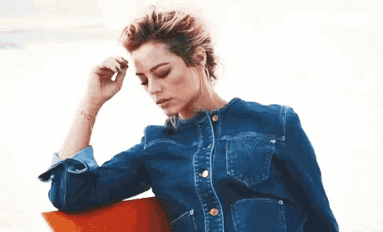 a woman in a denim jacket is sitting on an orange chair