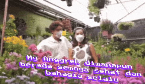 a man and woman wearing face masks are standing in front of flowers