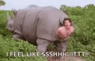 a man is standing next to a rhinoceros in a field and says `` i feel like sshhh ! ''