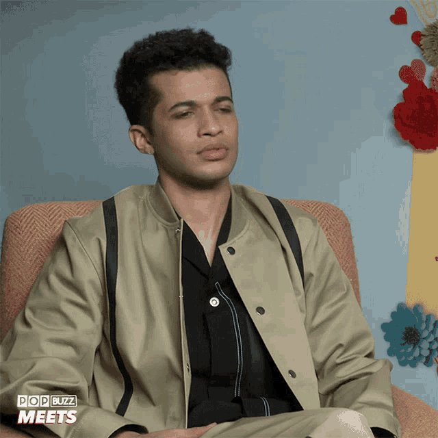 a man is sitting in a chair with the words pop buzz meets on the bottom of his jacket