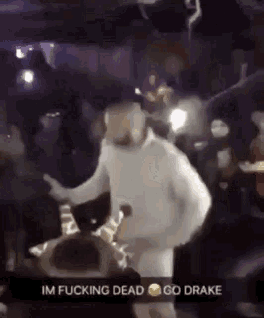 a man in a white sweater is dancing in front of a crowd in a club .