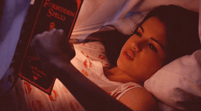 a woman is laying in bed reading a book called forbidden spells