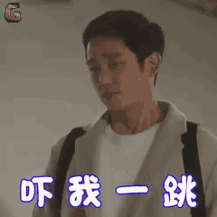 a man wearing a white shirt and a white jacket is standing in front of a wall with chinese characters on it .