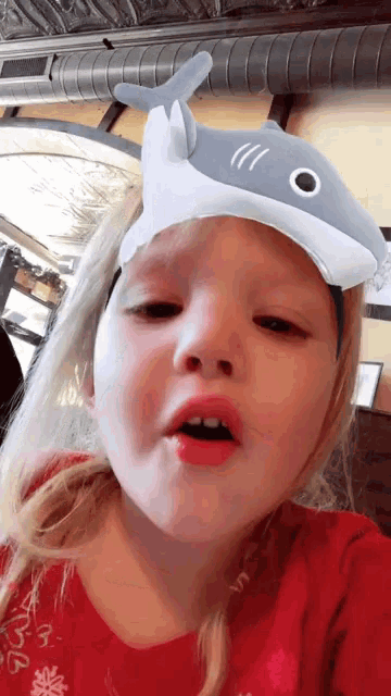 a young girl wearing a shark headband looks at the camera