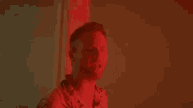 a man in a hawaiian shirt is standing in front of a red wall .