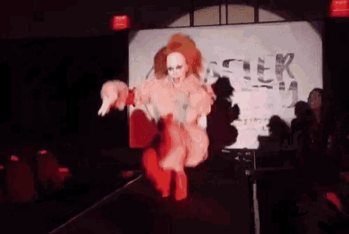 a drag queen is walking down a runway in front of a large screen that says easter