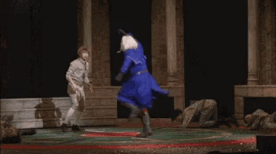 two people are dancing on a stage and one of them is wearing a blue coat .