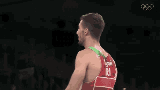 a wrestler is pointing up with the olympics logo behind him