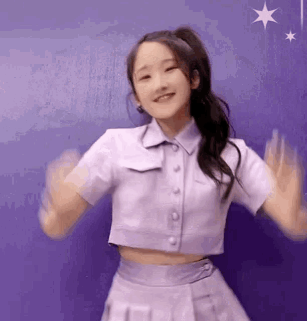a girl in a purple crop top and skirt is dancing in front of a purple wall .