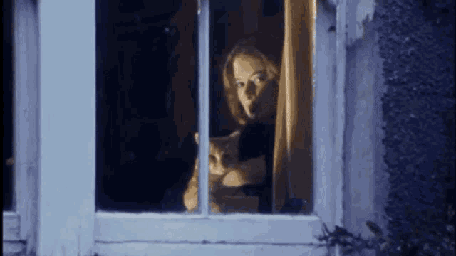 a woman is holding a cat in her arms while looking out of a window