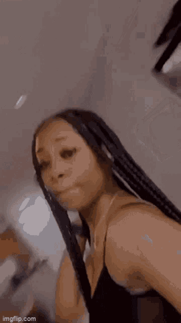 a woman with braids is taking a selfie in front of a mirror in a room .