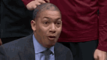 a man in a suit and tie is laughing while sitting in a stadium .