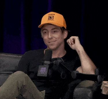 a man wearing an orange hat with the word aaron on it sits in front of a microphone