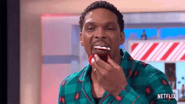 a man in a green plaid shirt is eating a candy cane donut with icing on it .