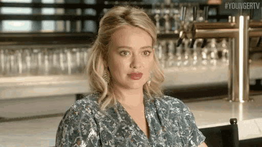 a woman is sitting at a table in front of a bar with glasses .